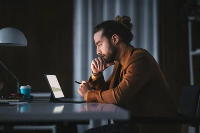 Foto van een thuiswerkende man die aandachtig naar zijn tablet kijkt met een pen in zijn hand.