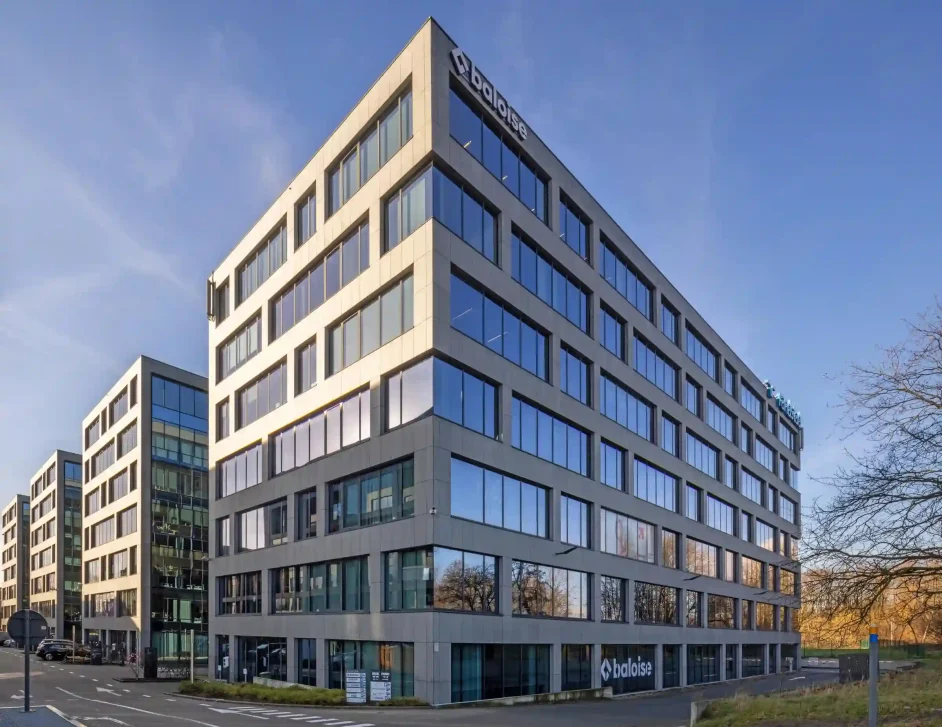 Foto van de buitenkant van het kantoorgebouw van Baloise in Antwerpen. Het is een rechthoekig pand van 7 verdiepingen opgetrokken uit grijze panelen en glas.