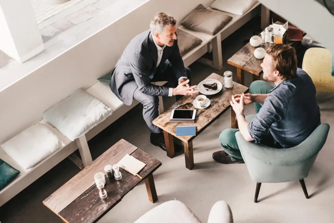 Foto met hoog standpunt, van 2 mannen die tegenover elkaar zitten en die een zakelijke bespreking voeren in een café.