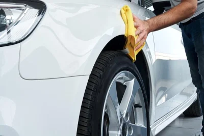 Close-up foto van een werknemer die het voorspatbord van een witte auto met een doek polijst.