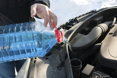 Close up van een man die de ruitensproeiervloeistof bijvult van zijn auto in de sneeuw.