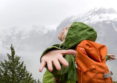 Foto van een vrouwelijke wandelaar met oranje rugzak, spreidt haar armen om de bergmist te omhelzen.