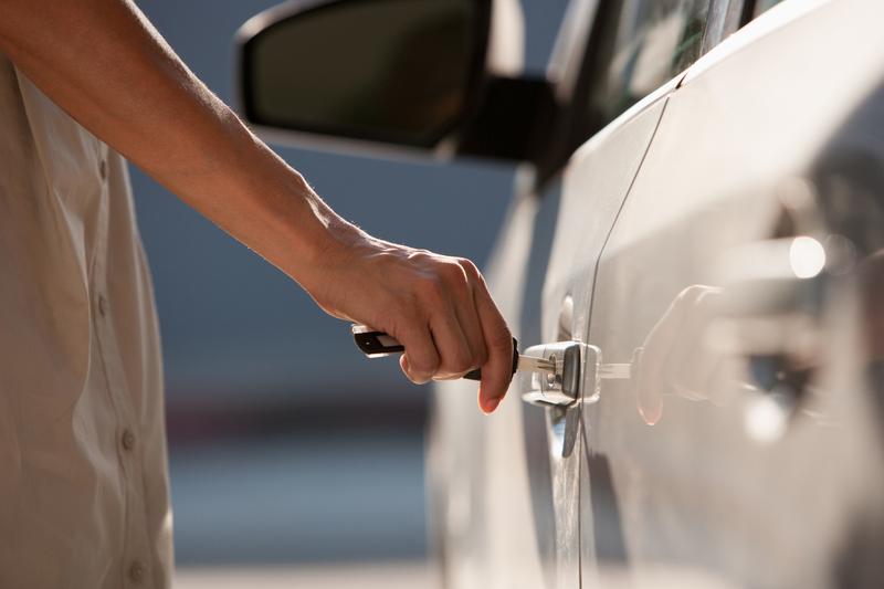 Close-up van een vrouw die de sleutel in het portier van haar auto steekt.