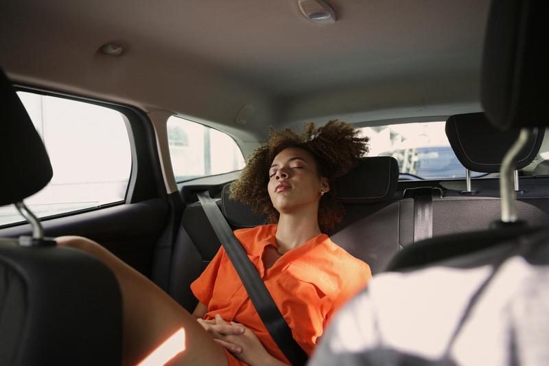 Foto van een afro-Amerikaanse vrouw die lekker ligt te slapen op de achterbank van een auto.