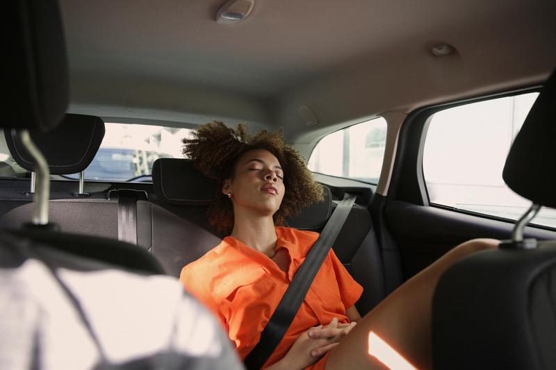 Foto van een afro-Amerikaanse vrouw die lekker ligt te slapen op de achterbank van een auto.