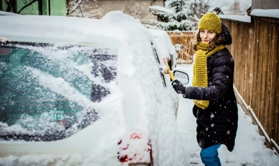 Foto van een vrouw die met een borstel haar auto sneeuwvrij aan het maken is.