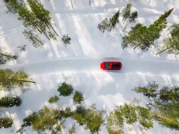 Luchtfoto van een rode auto met een zwarte dakkoffer die door het witte sneeuwlandschap van een winterbos rijdt op een landweg in Finland, Lapland.