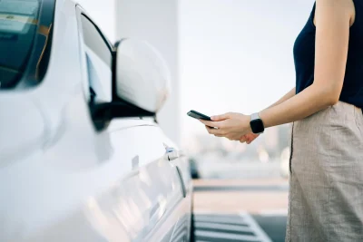 Close up van een vrouw die met haar telefoon haar witte auto aan het openen is.