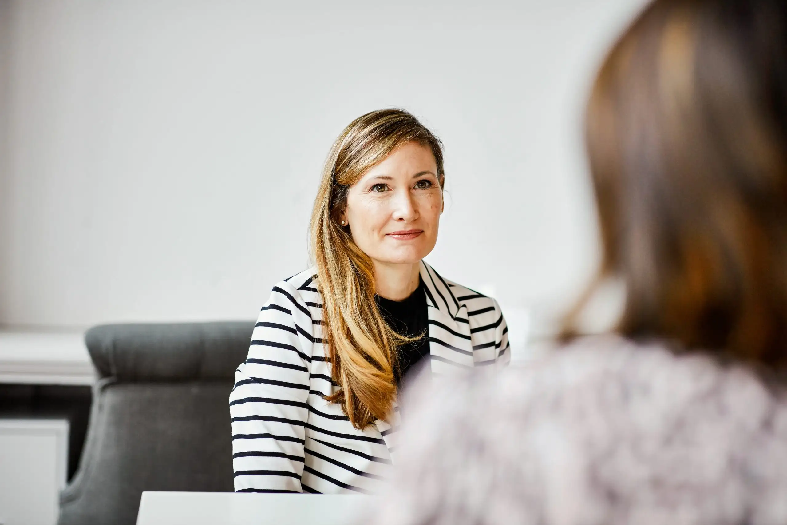 Foto van een vrouw die aandachtig luistert naar een collega die tegenover haar zit.