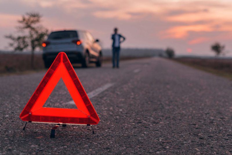 Sfeerfoto van gevarendriehoek met auto met pech en persoon op de achtergrond