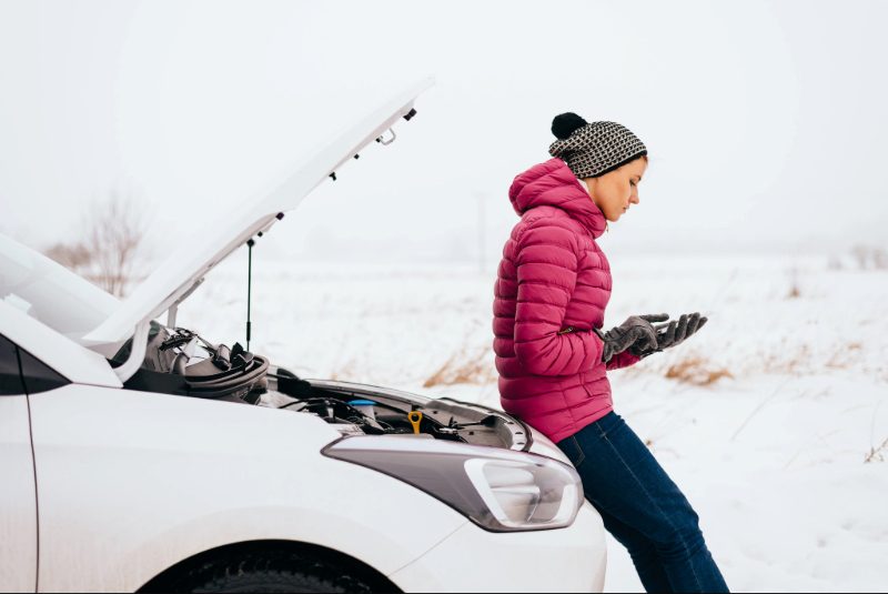 Vrouw met autopech is aan het SMS'en bij haar auto met de motorkap open.